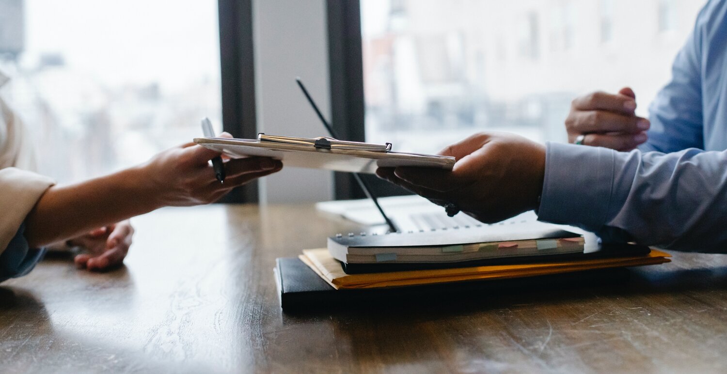 Close up of a man's and a woman's hands holding a clipboard between them over a desk